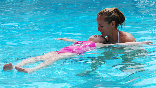 instructor helping a small girl float in pool