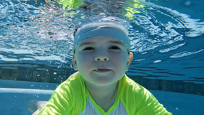 kind underwater holding breath wearing gray swim cap