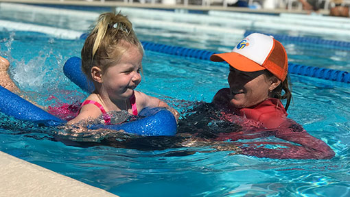 young girl with flotation device in pool with instructor