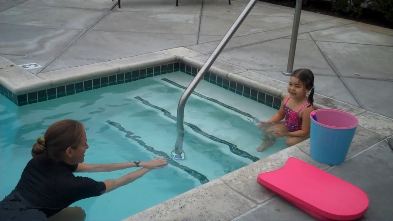 instructor helping a small girl float in pool